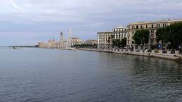 Bari city displaying its promenade and historic architecture along the calm adriatic sea, featuring a prominent ferris wheel and coastal buildings under a bright sky